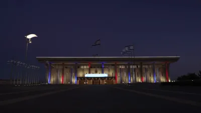 די כנסת געביידע באלייכט מיט די קאלירן פון די אמעריקאנער פאן