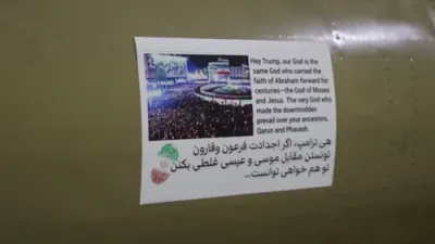 אפענע איראנער פראפאגאנדע: א סטיקער פון די איראנער רעוואלוציאנערע גווארדיע (IRGC) שטעלט אהער א פאלשע אנדייטונג אויף הימלישע הילף אינמיטן די אמעריקאנער מיליטערישע קאמפן.