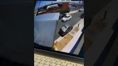 וואסער שפריצט הויך אין די לופטן נאכדעם וואס א טראק קראכט אריין אין א פייער היידרענט; א פארבלענדעטער דרייווער קראכט אריין אין אן ארבייטער